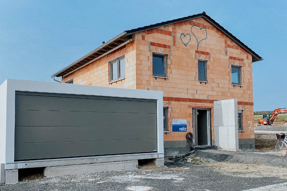 wissensratgeber-bauphase-grundstueck Einfamilienhaus im Rohbau von Schopf & Teig mit Garage und bereits eingesetzten Fenstern.